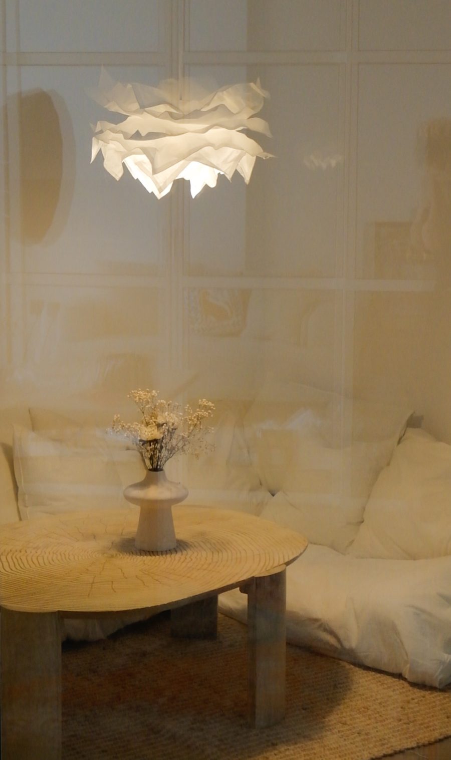 A paper pendant lamp glowing above a round wooden table with dried flowers and floor cushions